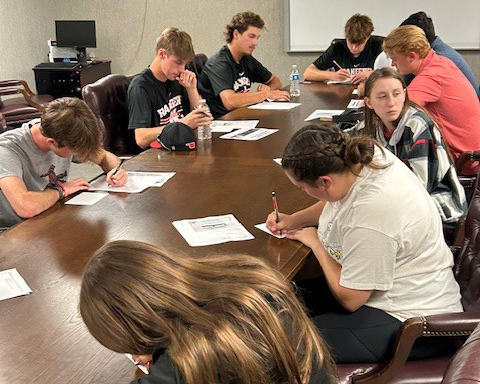 PLC students writing notes to Alva first graders while in class at a long conference table.