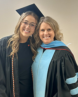 Dr. Summer Foster in black doctoral gown with light blue hood trim standing beside her daughter Mary Kate Foster in black graduation cap and gown with honor cords, who graduated with Bachelor of Science in Education from Northwestern Oklahoma State University.