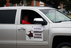 Man in red jacket seated in the driver's seat of a silver pickup truck. A magnetic sign on the door reads 