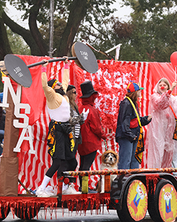 Students in costumes stand on a red-and-white circus-themed parade float marked 