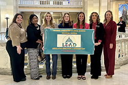 Seven members of the Northwestern Oklahoma State University Department of Social Work stand in a line in the marble rotunda of the Oklahoma State Capitol, holding a teal banner reading 