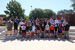 Students and staff from the 2026 Renewable Energy STEM Camp pose for a group photo on the steps of the Charles and Jane Tucker Ranger Plaza at Northwestern Oklahoma State University in Alva, Oklahoma. Participants are wearing matching navy and white camp caps. June 14-19, 2026.