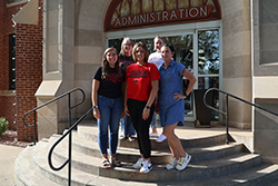 Five Northwestern Oklahoma State University employees, members of the Red-Hot Chili Steppers walking team, smile together on the steps outside the Administration Building on the Alva campus. Back row, left to right: Cheryl Ellis and Stacy Sanborn. Front row: Alexa Yost, Tara Hannaford and Jaime Johnson.