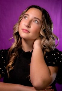 Kirstin Fennema, Miss Northwestern’s Teen contestant, in a black top, resting her chin on her hand in front of a purple backdrop.