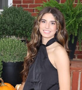 Jayla Adams, Miss Northwestern contestant, in a black halter top, seated beside potted plants and pumpkins on brick steps.