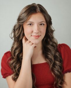 Hannah Hensley, Miss Northwestern’s Teen contestant, in a red top, resting her chin on her hand, against a gray background.