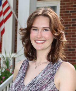 Jadyn Chancey, Miss Northwestern contestant, in a patterned sleeveless top, in front of a brick building with an American flag.