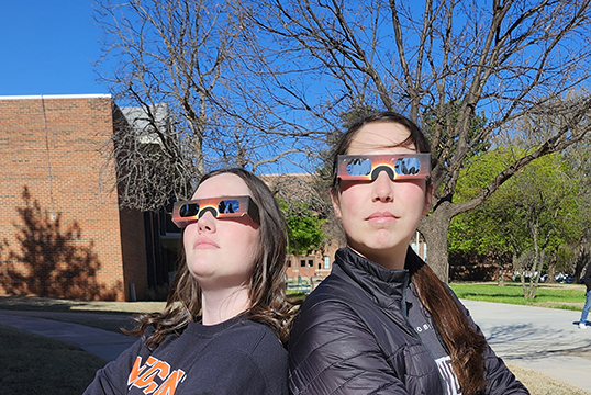 Northwestern senior biology majors Katy Brashears of Beaver and Jillian Bouse of Woodward try out a pair of eclipse glasses to get ready for the April 8 solar eclipse. The Department of Natural Sciences will be handing out about 700 free pairs of glasses at the viewing event at the Greenspace on the Northwestern-Alva campus.
