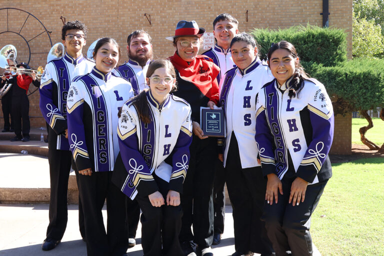Laverne High School band members in purple and white uniforms hold a plaque reading “Northwestern Oklahoma State University Homecoming Parade, October 10, 2026, 1st Place 2A Marching Band” at the Alva bandstand.