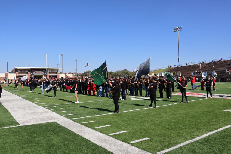 Color guard members wave green and silver flags in front of a long line of high school and middle school band students and the Ranger Marching Band on Ranger Field at Northwestern Oklahoma State University in Alva, Oklahoma.