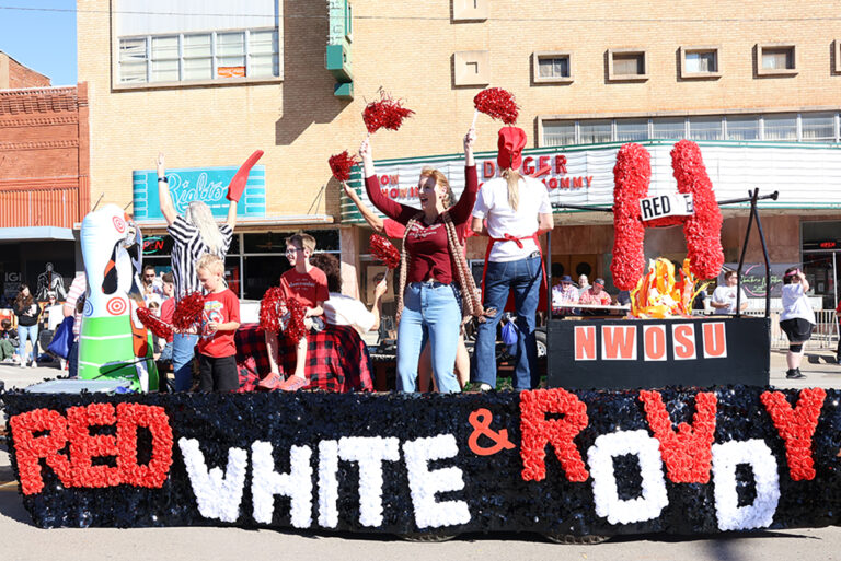 Riders cheer and wave red pompoms from the Dream First Bank float, decorated with the words “Red, White & Rowdy” and an NWOSU sign, during the Northwestern Oklahoma State University homecoming parade in downtown Alva, Oklahoma.