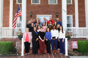 Students, faculty and benefactors of the Wisdom Family Foundation Doctoral Program for Rural Nursing Practice stand in four rows on the steps of the President’s House at Northwestern Oklahoma State University in Alva, Oklahoma, with an American flag at left.