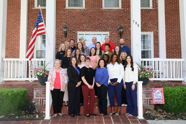 Students, faculty and benefactors of the Wisdom Family Foundation Doctoral Program for Rural Nursing Practice stand in four rows on the steps of the President’s House at Northwestern Oklahoma State University in Alva, Oklahoma, with an American flag at left.