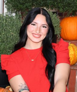 Isabella Nicholas, Miss Northwestern contestant, in a red ruffled-sleeve top, seated in front of pumpkins and greenery.