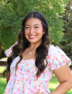 Mia Ovalle, Miss Northwestern contestant, in a pink floral top, standing outdoors in front of trees.