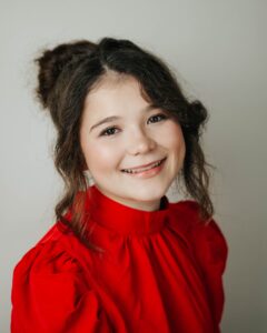 Rebecka “Becky” Carlson, Miss Northwestern’s Teen contestant, in a red high-neck blouse, against a gray background.