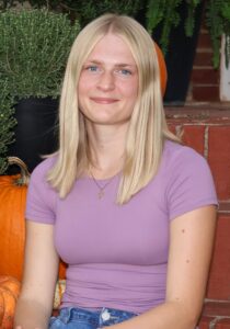 Jaidyn Frantz, Miss Northwestern contestant, in a lavender top, seated on brick steps with pumpkins.