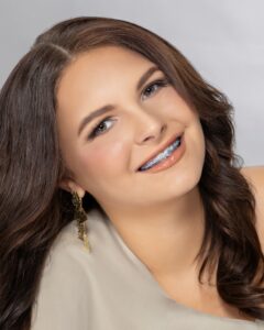 Paizley Green, Miss Northwestern’s Teen contestant, in a light top and gold earrings, against a gray background.