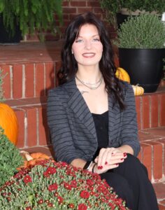Tatim Miller, Miss Northwestern contestant, in a gray blazer, seated on brick steps beside red mums and pumpkins.