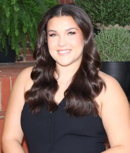 Raegan Bleything, Miss Northwestern contestant, in a black sleeveless top, seated in front of brick steps and potted plants.