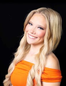 Jaci Adee, Miss Northwestern’s Teen contestant, in an orange off-the-shoulder top, against a black background.