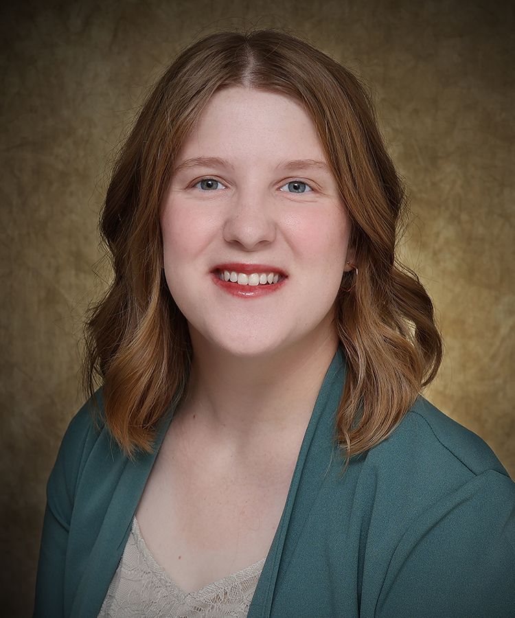 Professional studio portrait of Isabella Burden, a young woman with shoulder-length wavy auburn hair, smiling and wearing a teal cardigan over a light-colored top, against a mottled brown and gold background.