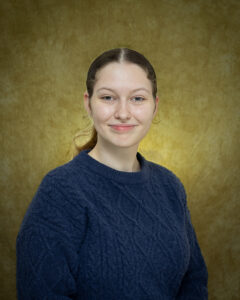 Belinda Garvie, Northwestern Oklahoma State University junior English major and spring 2027 Brad Henry International Scholar, smiles in a navy blue cable-knit sweater in front of a mottled tan studio backdrop