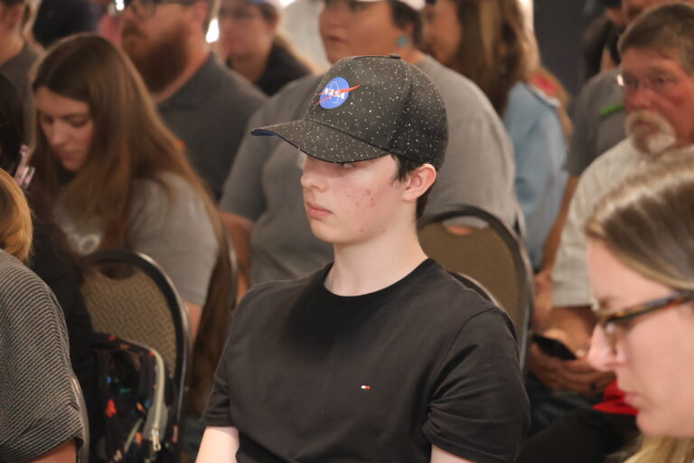A Northwestern student in a black cap bearing the blue NASA insignia listens during the campus presentations in the Student Center Ballroom.