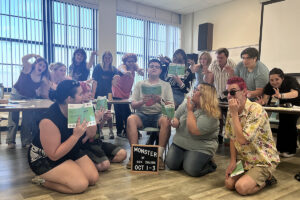• Northwestern Oklahoma State University theatre students pose in exaggerated monster poses with clawed hands and startled faces during a rehearsal for “Monster” in Ryerson Hall. Several hold green scripts, and a letterboard sign on the floor in front of them reads “Monster by Don Zolidis Oct 1-3.”