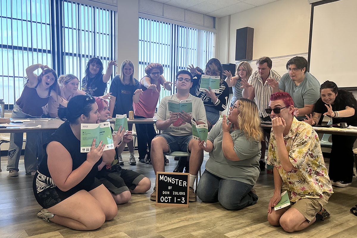 • Northwestern Oklahoma State University theatre students pose in exaggerated monster poses with clawed hands and startled faces during a rehearsal for “Monster” in Ryerson Hall. Several hold green scripts, and a letterboard sign on the floor in front of them reads “Monster by Don Zolidis Oct 1-3.”