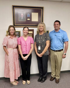 Four people stand together in front of a wall with a large framed portrait display, smaller framed photos and a wooden plaque at Bill Johnson Correctional Center. From left: Dr. Kylene Rehder, chair of the Northwestern Oklahoma State University Department of Social Work; Haylee Durrence, Northwestern junior social work major and practicum student at the correctional center; Becky Guffy, warden of Bill Johnson Correctional Center; and Trent Spade, treatment director at the correctional center.