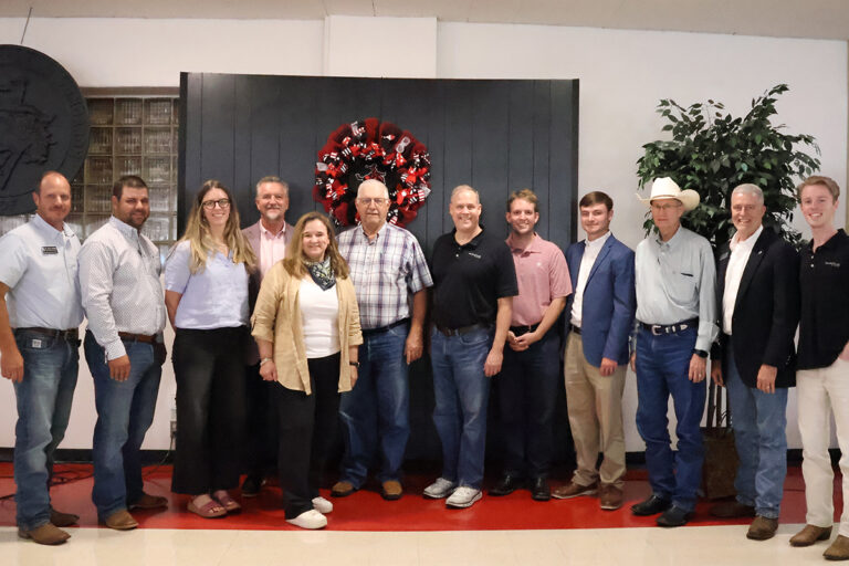 Twelve people stand together in the Student Center Ballroom at Northwestern Oklahoma State University in front of a red and black wreath bearing the Northwestern Ranger logo. The group includes NASA and NASA Acres leaders alongside Oklahoma state legislators, congressional staff and federal agency officials who attended the campus presentations.