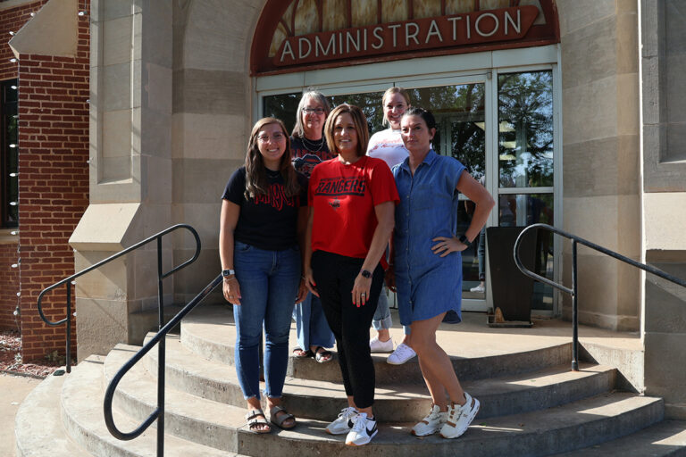 Five Northwestern Oklahoma State University employees, members of the Red-Hot Chili Steppers walking team, smile together on the steps outside the Administration Building on the Alva campus. Back row, left to right: Cheryl Ellis and Stacy Sanborn. Front row: Alexa Yost, Tara Hannaford and Jaime Johnson.