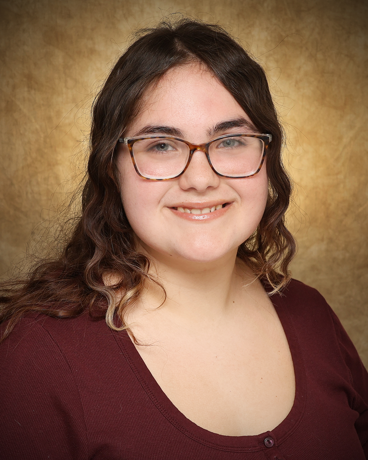 Jacie Willson, a Northwestern Oklahoma State University Upward Bound Math Science student, smiles in a portrait wearing a brown blouse against a mottled gold backdrop.